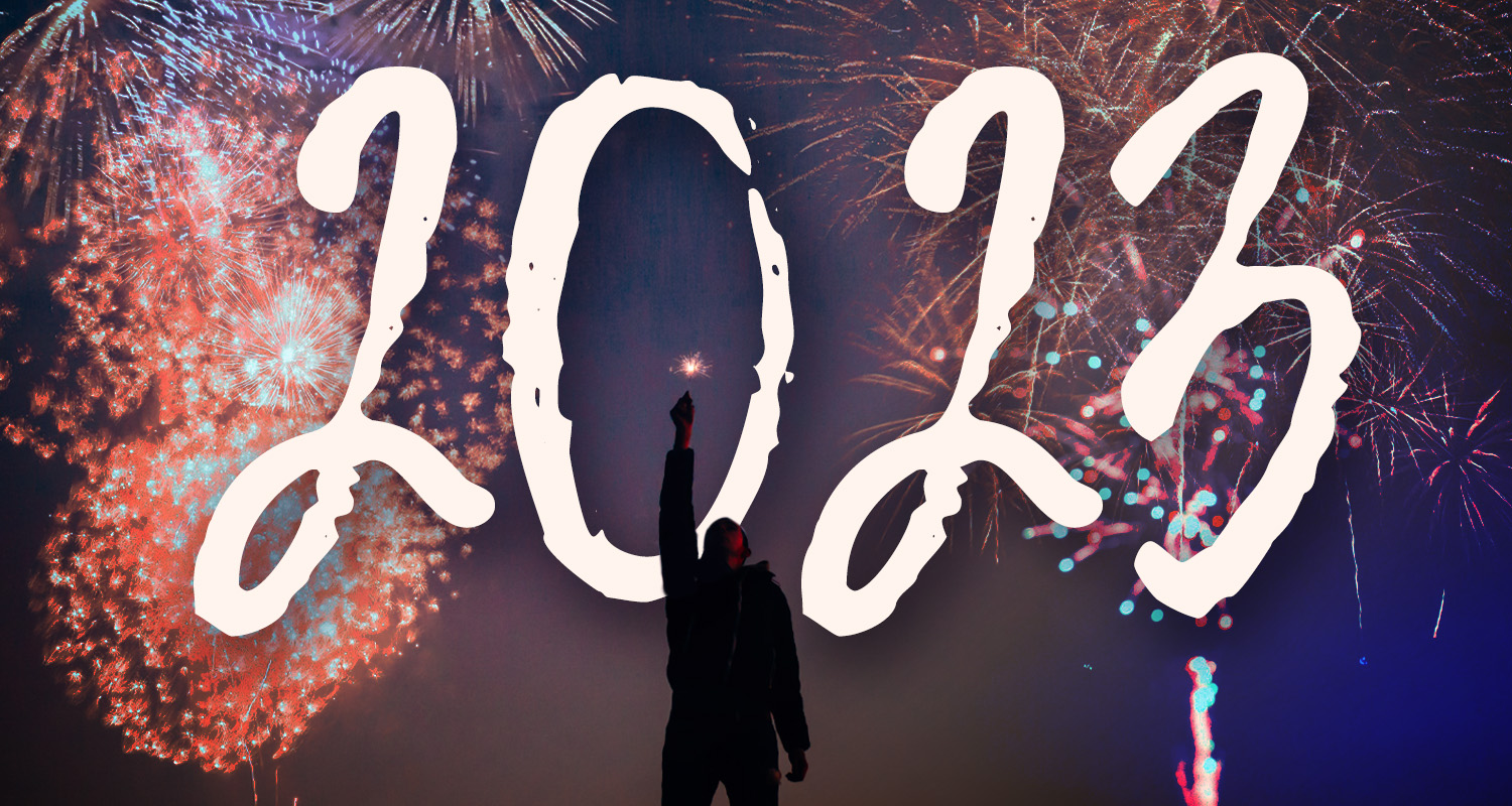 person holding sparkler under fireworks with the letters 2023 over image